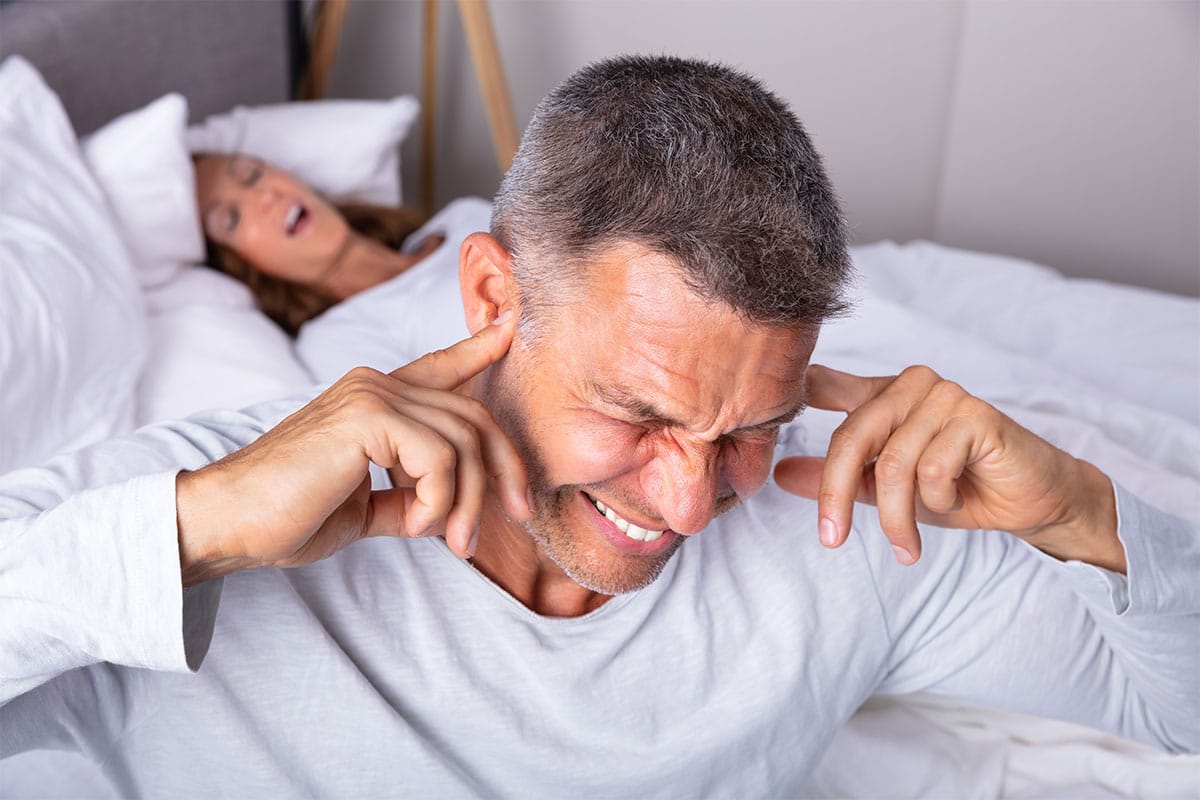 Man using fingers as earplugs for snoring.