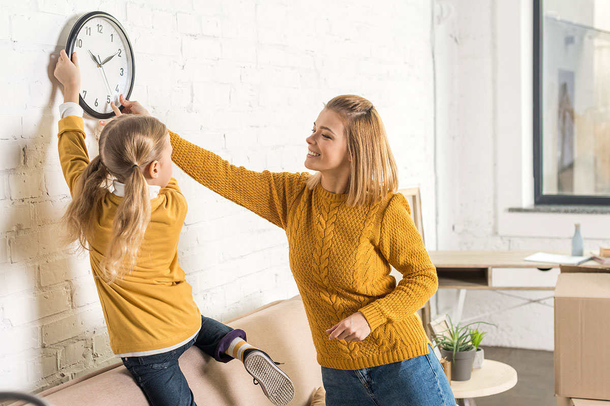 Woman and daughter adjusting clock for daylight savings time.