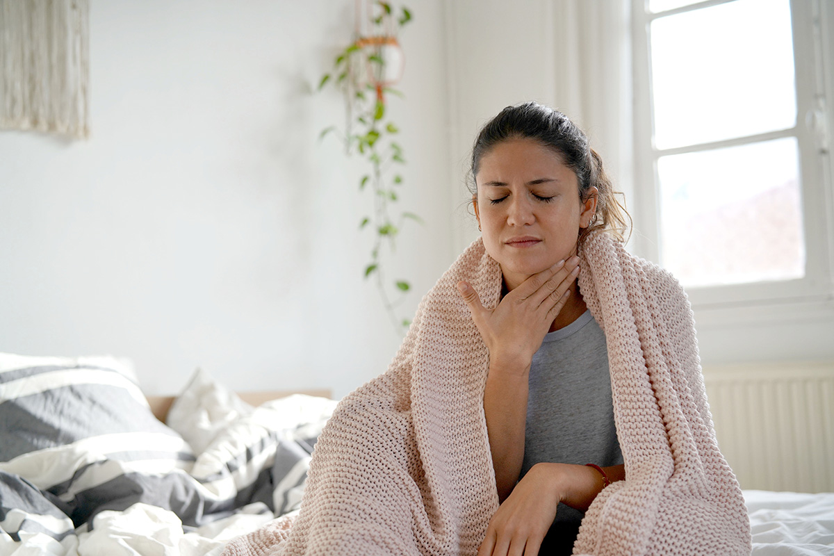 Woman with sore throat in bed wondering if snoring can damage your throat