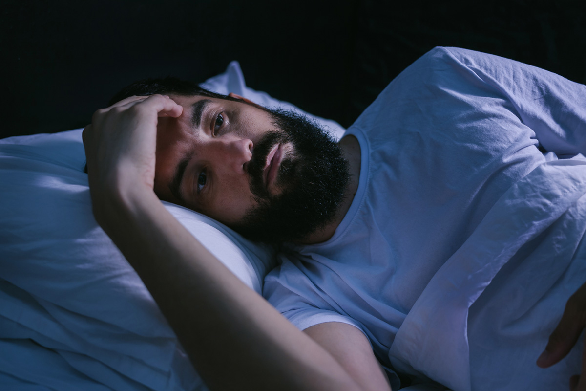 Man in bed late at night suffering from a sleep disorder.